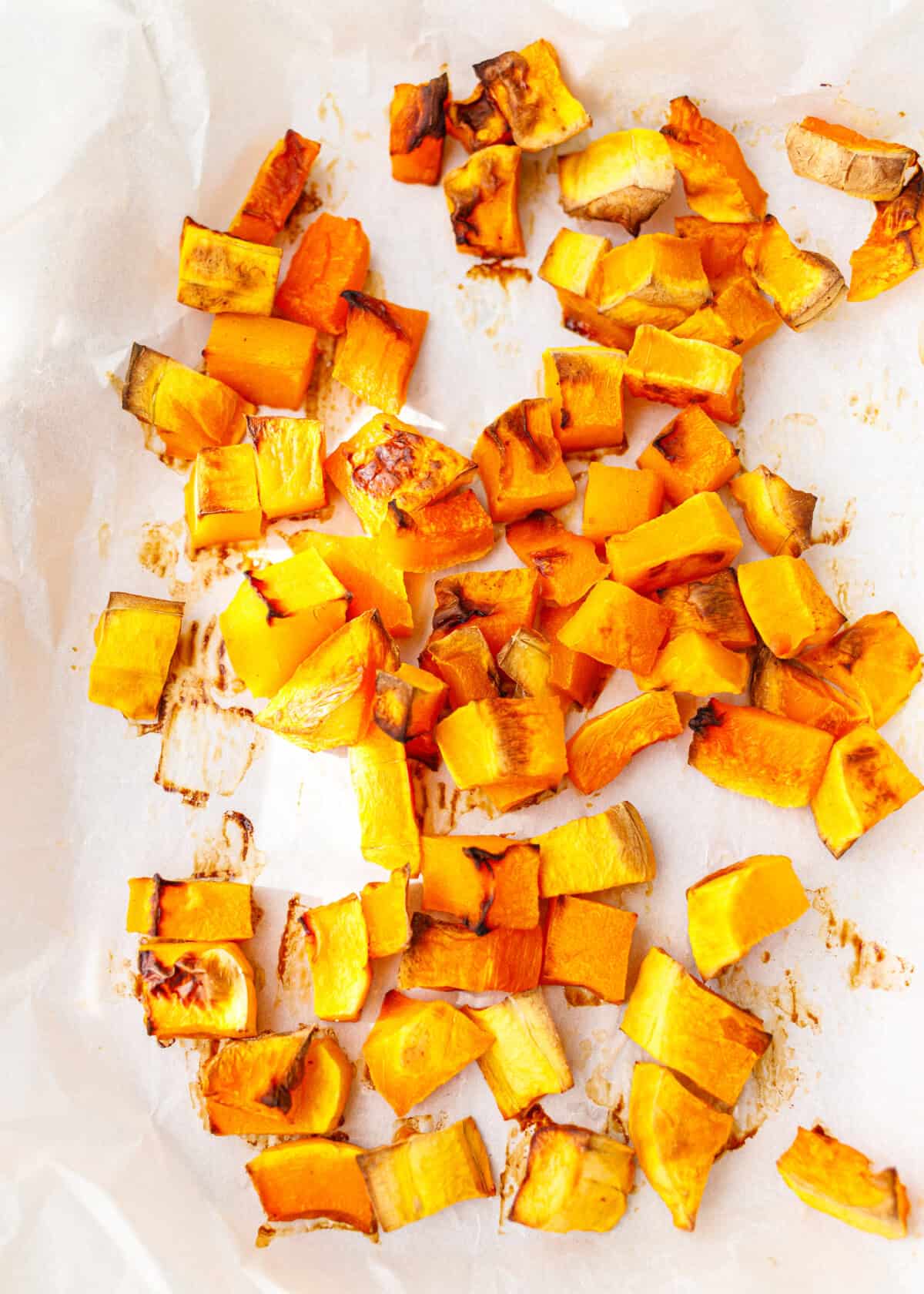 Roasted pumpkin cubes with caramelized edges on a parchment-lined baking sheet.