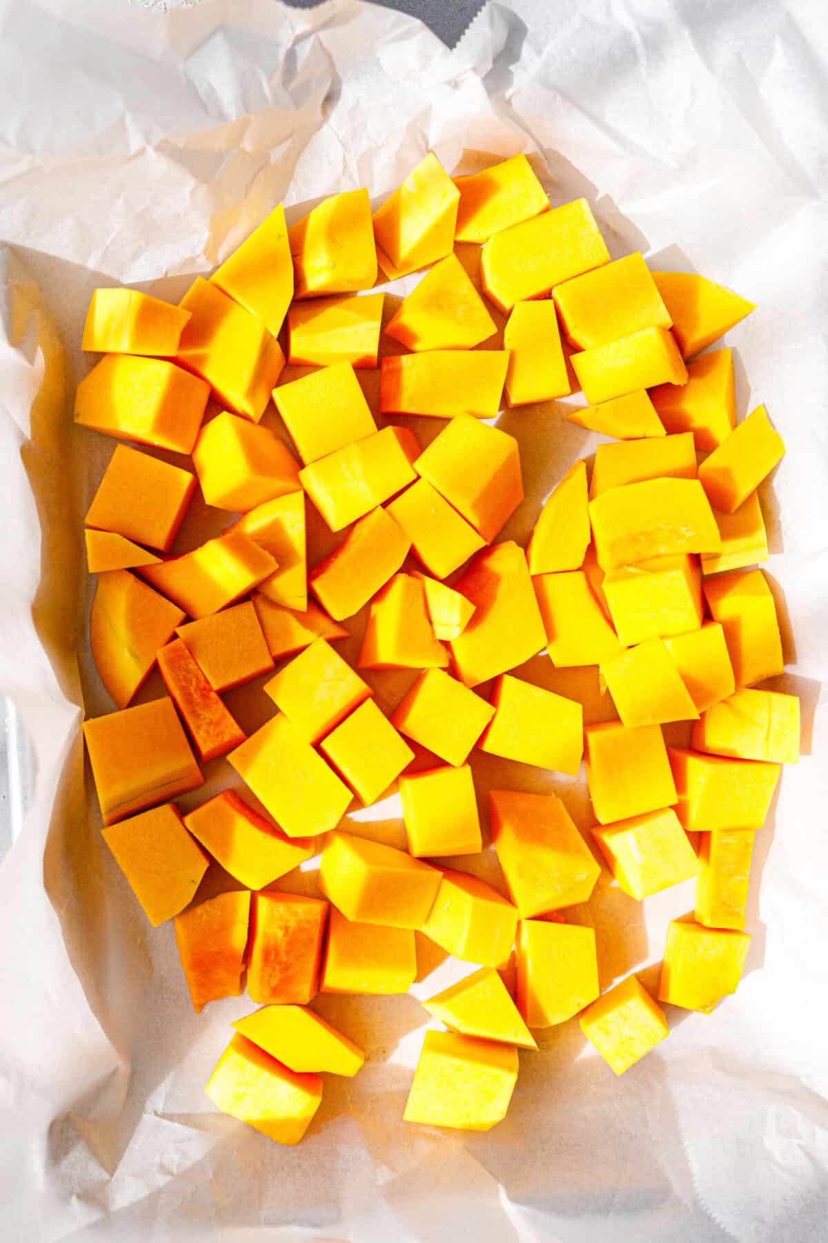 Raw peeled pumpkin cubes spread on parchment paper.
