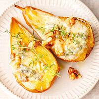 Two savory baked pear halves with melted blue cheese, walnuts and fresh thyme on a white ceramic plate