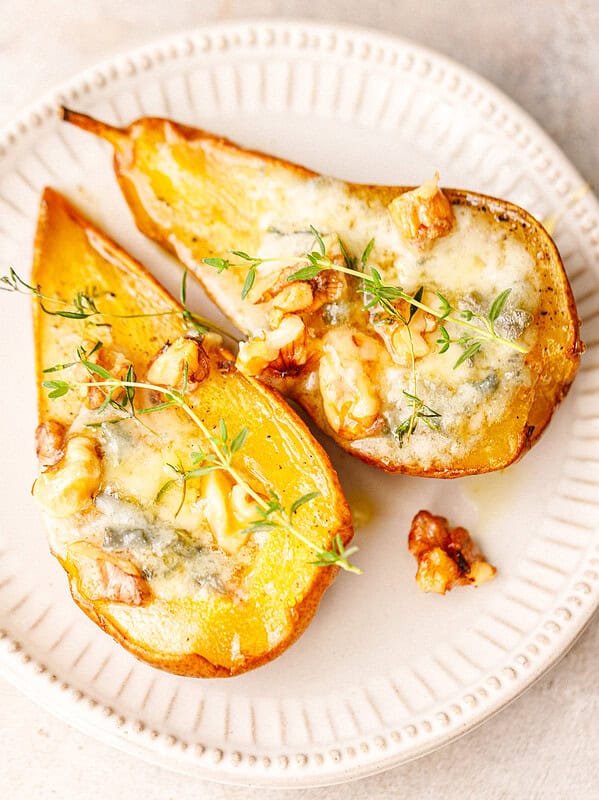Two savory baked pear halves with melted blue cheese, walnuts and fresh thyme on a white ceramic plate