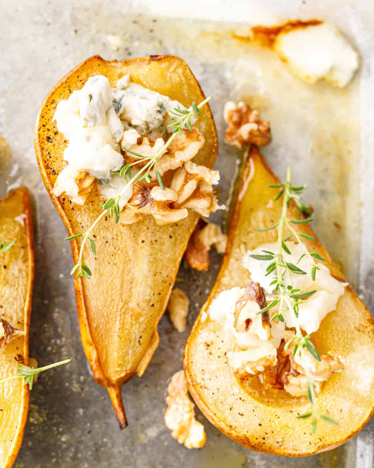 Close-up of baked pears topped with crumbled blue cheese, walnuts and fresh thyme in a baking dish