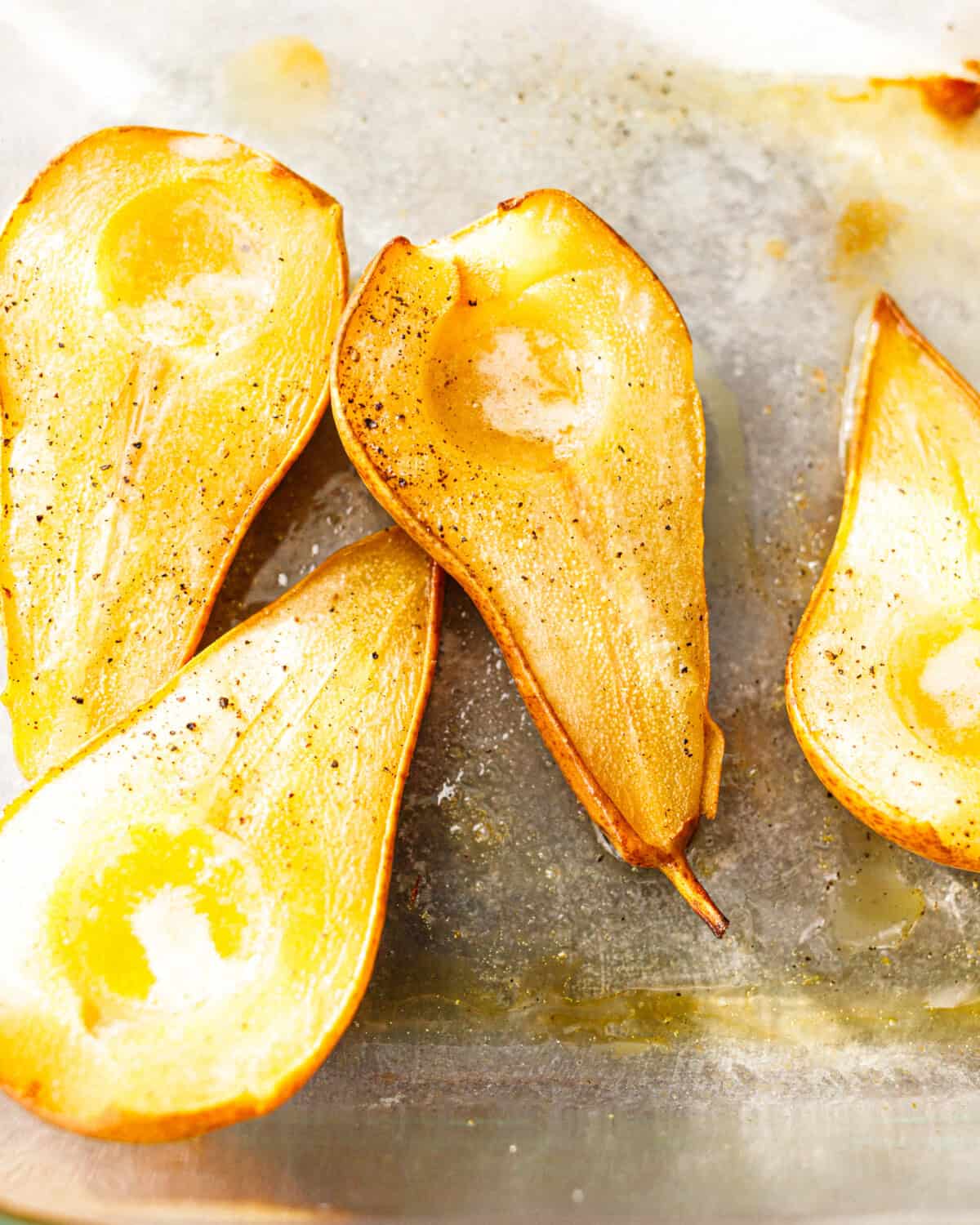 Golden caramelized baked pear halves seasoned with black pepper in a glass baking dish