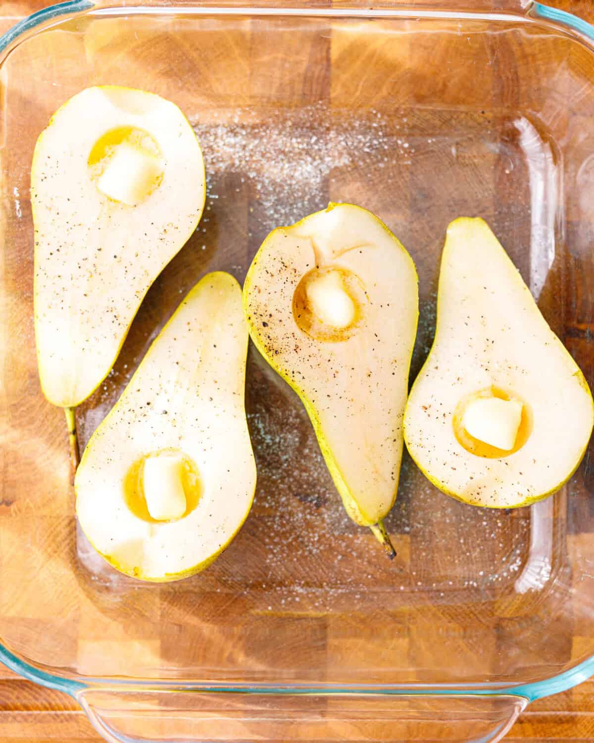 Halved cored pears seasoned with salt and black pepper, with a cube of butter in each hollow, in a glass baking dish