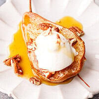 Baked pear half topped with Greek yogurt, chopped pecans and honey on a white scalloped plate