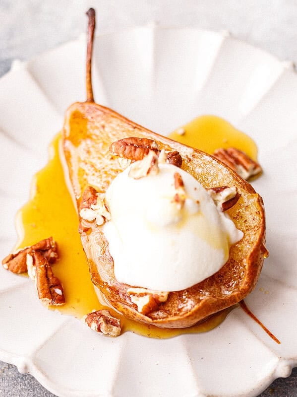 Baked pear half topped with Greek yogurt, chopped pecans and honey on a white scalloped plate