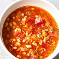 Close-up of crockpot white bean soup with whole white beans, tomatoes, roasted red pepper and parsley