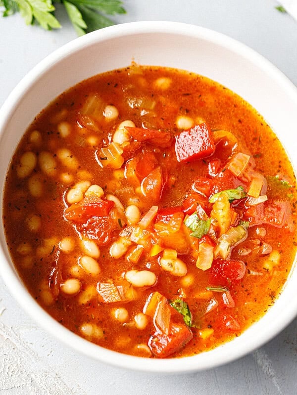 Close-up of crockpot white bean soup with whole white beans, tomatoes, roasted red pepper and parsley